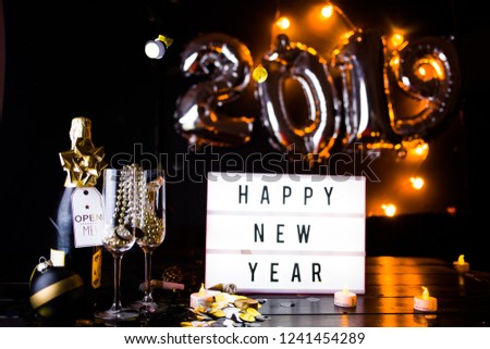 New Years Eve celebration conceptual photo, with christmas decoration in golden tone, a bottle of champagne with a small card texting open me, and in the background,2019 made with inflatbale ballots.
