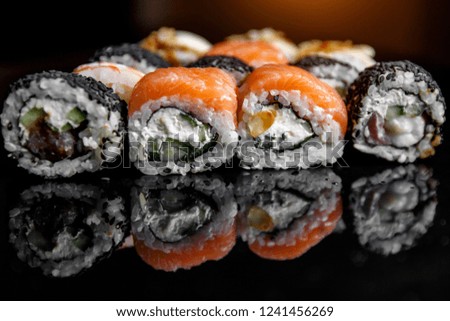Sushi rolls with salmon, tuna, cucumber and green onions on black background, with reflection
