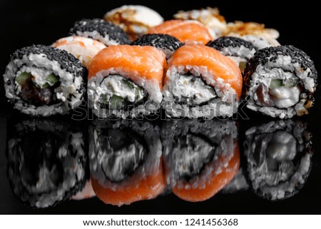 Sushi rolls with salmon, tuna, cucumber and green onions on black background, with reflection