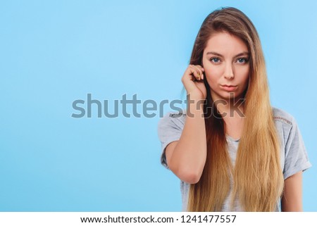 Girl in gray clothes on a blue background touches the ear. Concept attentive, body language, sign, distraction attention. Copy space left. Closeup. 