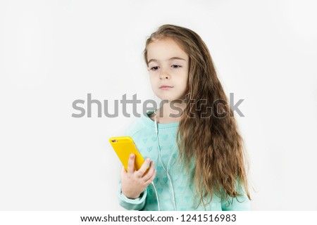 Bright beautiful little girl in headphones offended with a phone in their hands on an isolated background.