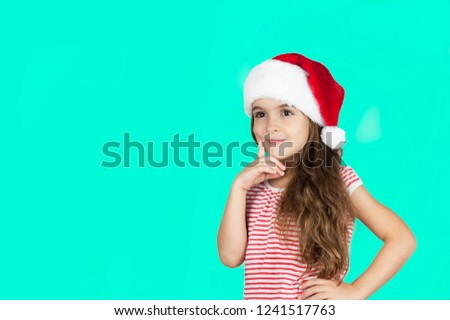 
Little bright beautiful girl emotionally posing in Santa hat on an isolated turquoise background