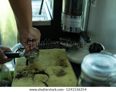 Hand of Barista presses ground coffee using tamper.