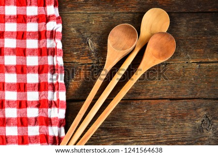 An image of wooden mixing spoons and a colorful table cloth on an old country kitchen table top. 