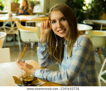 Indoor portrait of pretty blond woman listening music and holding mobile phone in the coffee shop.
