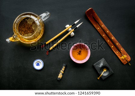 Chinese or japanese traditions. Calligraphy and tea ceremony concept. Special writting pen, ink near teapot and cup of tea, insense on black background top view