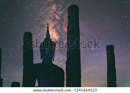 Abstract vintage tone long exposure photography of The Ancient Buddha statue in Sukhothai Historical park, Thailand in the night time with milky way and stars on the night sky background.