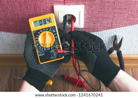 Electrician worker measures the voltage in the outlet with a multimeter. Electricity works concept.