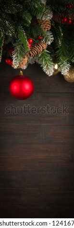 Christmas background with fir tree green branches, greeting card with decoration in red and golden colors on dark brown wooden board, copy space banner