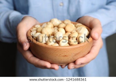 Woman holding bowl with shelled organic Macadamia nuts, closeup