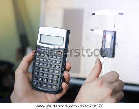 In the hands of an engineer, a calculator and a caliper on the background of drawings on a computer. Concept engineer, high measurement accuracy, production, manufacturability, design, engineering, in
