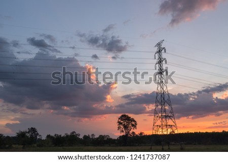 High voltage electricity transmission pylon silhouette with power plant against dark lights sky.