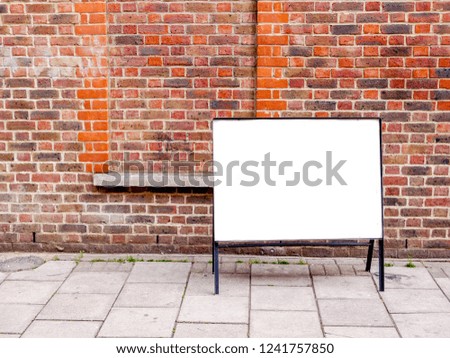 Blank white canvas ad board in front in front a red brick wall on city pavement.
