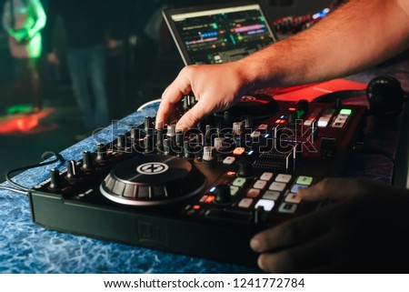 hands of a DJ in a booth playing on the mixer in the club