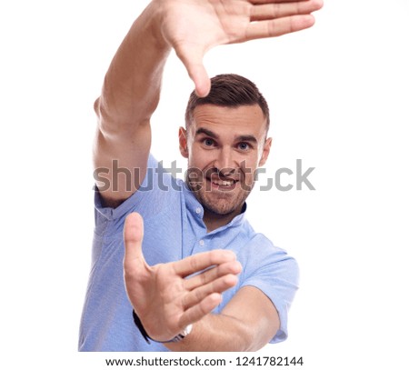 Cheerful satisfied unshaven man makes frame sign with both hands, prepares for being photographed, dressed in casual red t shirt, stands against white background. Look at life from bright angle