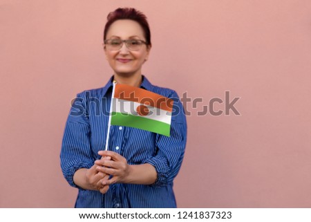 Niger flag. Middle aged woman 40 50 years old holding national flag over pink wall on the street outdoors. Selective focus on the flag.