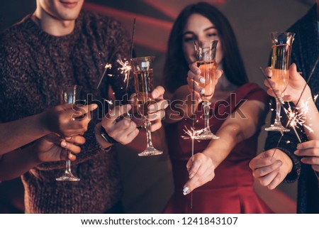 Well dressed. Multiracial friends celebrate new year and holding bengal lights and glasses with drink.