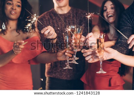 Rejoice as in childhood. Multiracial friends celebrate new year and holding bengal lights and glasses with drink.