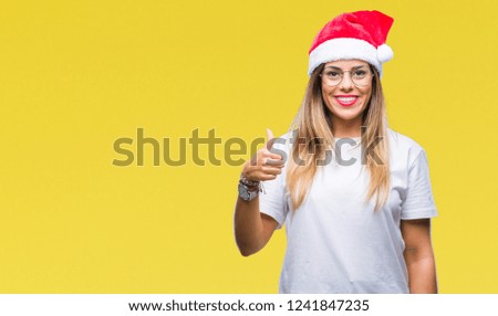 Young beautiful woman wearing christmas hat over isolated background doing happy thumbs up gesture with hand. Approving expression looking at the camera with showing success.