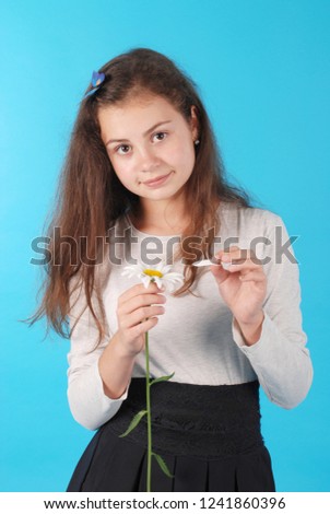 Young girl guesses on a chamomile flower. Young girl tears off petals of daisy. Isolated on blue background in studio