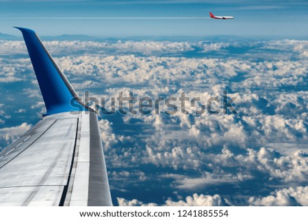 Two commercial airplanes (aircraft wing and plane) while flying above the clouds