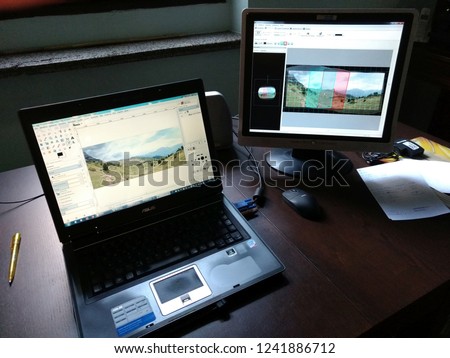 A portable laptop computer with another monitor connected, on an office desk with a pen and papers, running Gimp and Hugin photo editing software