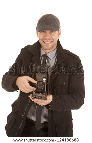 A man with a smile on his face holding on to a antique camera taking a picture.