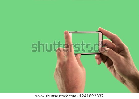 The guy takes pictures or shoots video on a mobile phone. Close-up of the hands of a man with a gadget on a green background. Chroma Key.