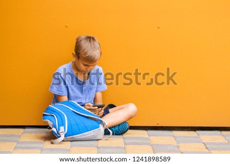 Boy with smartphone sitting on the ground near colorful wall