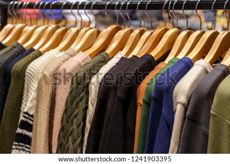 Multicolored woolen knitted sweaters hanging on hangers close-up, side view