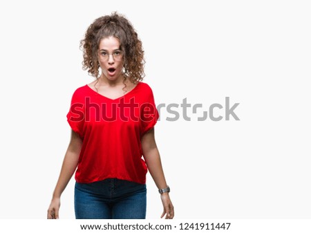 Beautiful brunette curly hair young girl wearing glasses over isolated background afraid and shocked with surprise expression, fear and excited face.