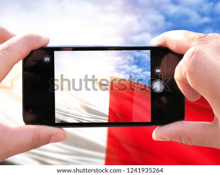 The hands of men make a phone photograph of the flag of malta