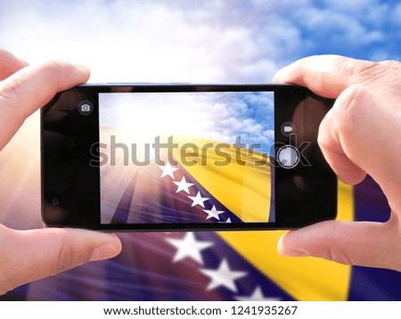 The hands of men make a phone photograph of the flag of Bosnia and Herzegovina