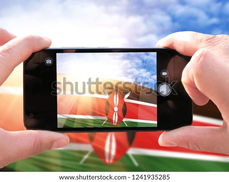 The hands of men make a phone photograph of the flag of Kenya
