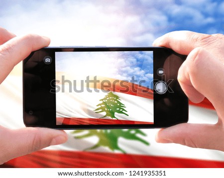 The hands of men make a phone photograph of the flag of Lebanon