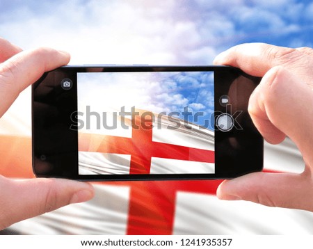 The hands of men make a phone photograph of the flag of England