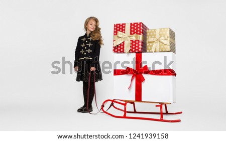 Cute little girl dressed in Santa Claus costume holding a sled.