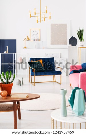 Plant on wooden table in white apartment interior with gold lamp above armchair. Real photo