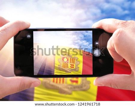 The hands of men make a phone photograph of the flag of Andorra