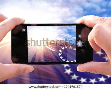The hands of men make a phone photograph of the flag of Cook Islands