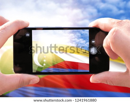 The hands of men make a phone photograph of the flag of Comoros