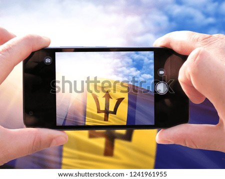 The hands of men make a phone photograph of the flag of Barbados