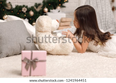 cute child girl playing with teddy bear at home and beatiful pink christmas gift box in the foreground