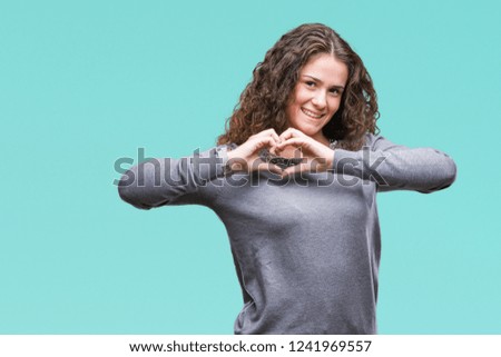 Beautiful brunette curly hair young girl wearing a sweater over isolated background smiling in love showing heart symbol and shape with hands. Romantic concept.
