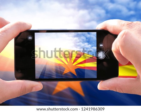 The hands of men make a phone photograph of the flag State of Arizona