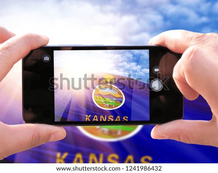 The hands of men make a phone photograph of the flag State of Kansas