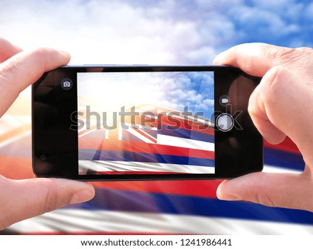 The hands of men make a phone photograph of the flag State of Hawaii