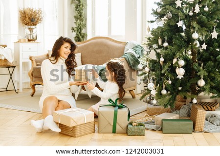 Family Christmas. Mom and daughter open or pack Christmas gifts at home in the living room.