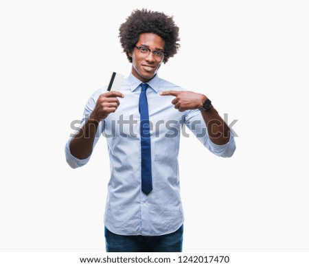 Afro american man holding credit card over isolated background with surprise face pointing finger to himself