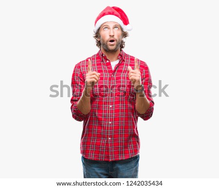 Handsome hispanic man model wearing santa claus christmas over isolated background amazed and surprised looking up and pointing with fingers and raised arms.